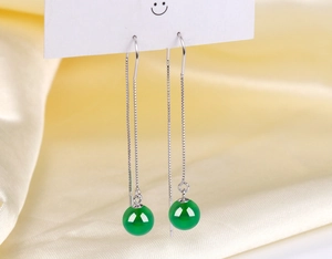 Close-up of long silver tassel earrings with round green agate beads on yellow silk cloth