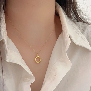 Close-up of minimalist gold teardrop pendant necklace worn by a model in a white shirt