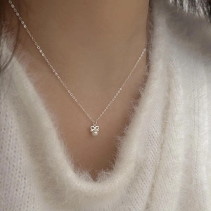 Detailed view of 925 silver bow necklace with white pearl on a white knit sweater