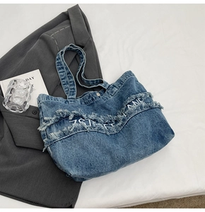 Détail du sac cabas en denim bleu avec bords effilochés et broderie de lettres