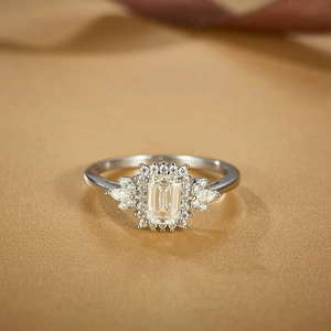 Emerald cut moissanite engagement ring in flower setting on beige fabric background