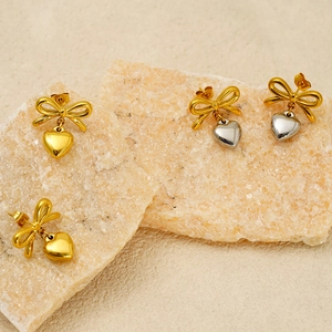 Détail de boucles d'oreilles nœud doré avec pendentifs cœur sur plaques de pierre