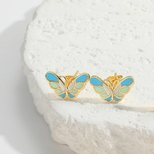 Detailed close-up of golden butterfly earrings with blue and green gradient enamel on white stone