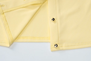 Détail du tricot côtelé jaune avec boutons sphériques métalliques et finitions de couture
