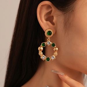 Detailed close-up of retro gold drop earrings with green gems and crystals on a model