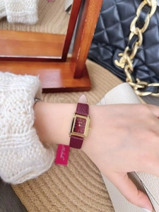 Detail of elegant rectangular gold watch with red leather strap on woman's wrist
