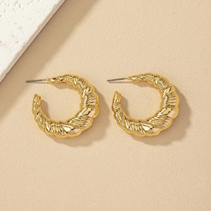 Detailed view of golden C-shaped hoop earrings with spiral twisted texture design