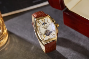 Detail of tonneau mechanical watch with gold case, moon phase display and leather strap