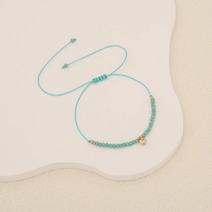 Macro shot of turquoise braided bracelet with faceted beads and a crystal heart pendant