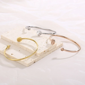 Minimalist adjustable C-shape bangle in gold, silver, and rose gold on a stone base
