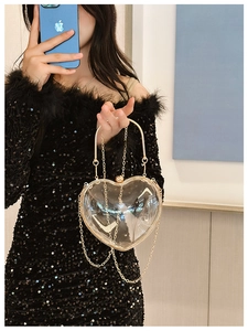 Mirror selfie showing the transparent heart-shaped acrylic crossbody bag with gold chain