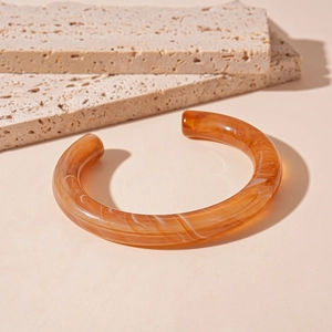 Detail of amber acrylic open bangle with white marble texture on beige stone