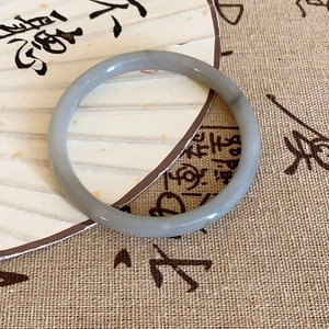 Close-up of polished grey stone bangle on a vintage calligraphy fan backdrop