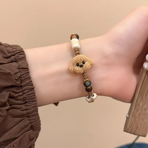 Close-up of a brown teddy dog charm on a woven wax cord bracelet with ceramic beads