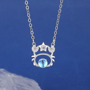 Macro shot of silver crab pendant with blue moonstone on a vibrant blue backdrop