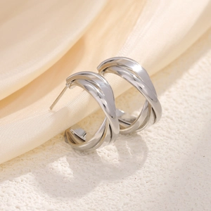Polished silver geometric multi-layer spiral earrings on a minimalist cream fabric background