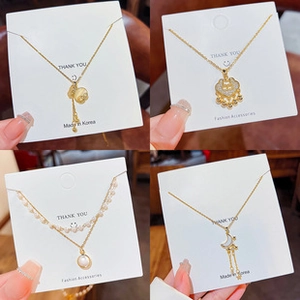 Detail of four gold necklaces featuring pearl, moon, and lock pendants on display cards