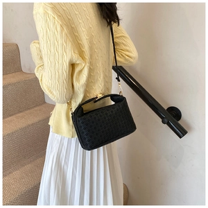 Fashionable black woven pillow bag with gold hardware shown on a staircase lifestyle setting