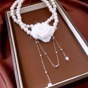 Detail of double-layer pearl necklace featuring a white crochet flower pendant and long tassels