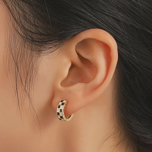 Fashionable black and white checkered hoop earrings in gold finish on female ear