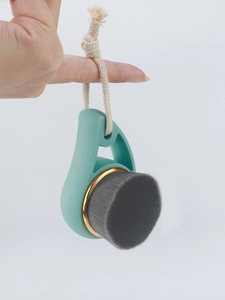 Detail of bamboo charcoal facial brush with mint green handle and golden ring with hanging rope