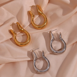 Detail of irregular U-shaped hollow earrings in gold and silver finish on silk fabric
