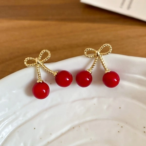 Macro detail of red resin cherry earrings with gold bowknot on a white porcelain dish