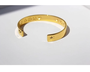 Detail shot of the gold-plated open bangle with engraved star patterns and polished finish