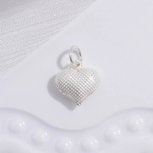 Macro shot of silver heart pendant with refined grid texture on white silk background