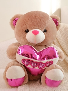Close-up of light brown plush bear holding a pink metallic LOVE heart pillow