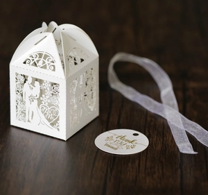 Macro detail of laser-cut white wedding favor box with Mr & Mrs text and silk ribbon
