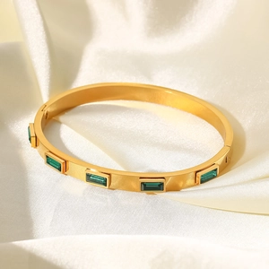 Détail d'un bracelet en acier doré 18 carats avec zircons verts sur un tissu en soie