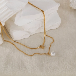 Detail of double-layer gold necklace featuring a sleek snake chain and elegant pearl pendant