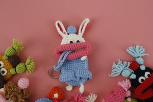 Detail of handmade crochet white bunny key pouch with pink lips and blue overalls