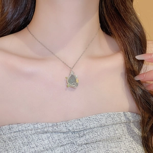 Macro shot of silver wire-wrapped green gemstone pendant on model's neck for elegant styling