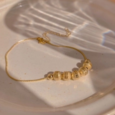 Close-up of gold planet bracelet on ceramic tray with elegant shadows and lobster clasp