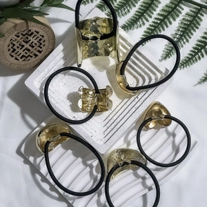 Golden metal hair ties with black elastic bands on a minimalist white stone tray