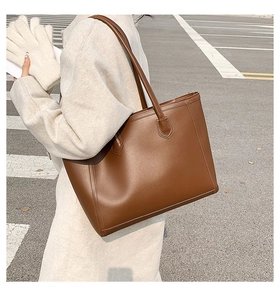 Brown leather tote bag shown in a street style setting over a woman's shoulder