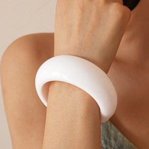 Detailed view of a wide thick white resin bangle with smooth glossy surface on a female wrist