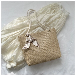Vue à plat d'un sac cabas en paille avec anses en corde et foulard sur tissu blanc