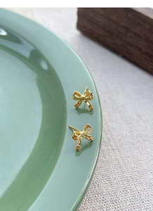 Close-up of golden bow-shaped S925 sterling silver stud earrings on ceramic tray