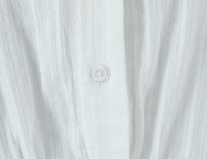 Macro view of white textured jacquard fabric with a clear button on the polo collar top