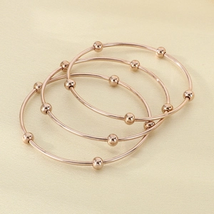 Detailed top view of three rose gold titanium bracelets with sliding beads on neutral background