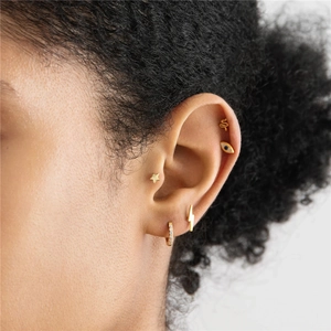 Detail view of model wearing gold star, lightning, and snake earrings set with zircons