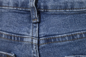 Macro detail of yellow contrast stitching and belt loop on blue denim straight leg pants