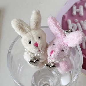 Close-up of cute plush bunny charms with pearl necklaces inside a glass cup