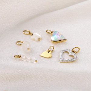 Selection of gold heart and star charms with pearl and crystal details on white fabric