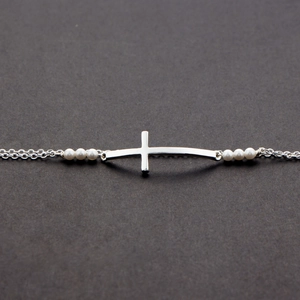 Detail of silver cross bracelet with polished freshwater pearls on dark textured background