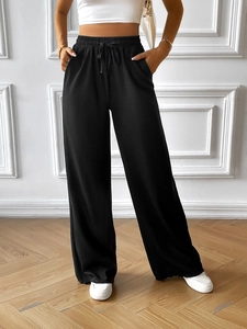 Detail of black wide-leg trousers featuring elastic waistband with drawstring and pockets
