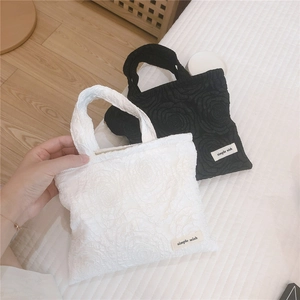 Detailed view of white rose embossed fabric handbag with brand label and handle